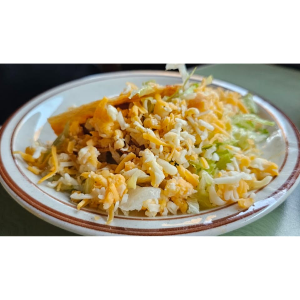 A Casa Mexico taco with shredded lettuce, white cheese, and yellow cheese on a white plate.