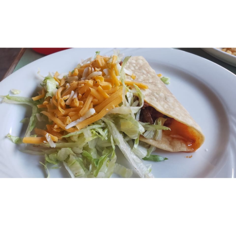 A soft taco with meat, lettuce, and shredded cheese, served on a white plate.