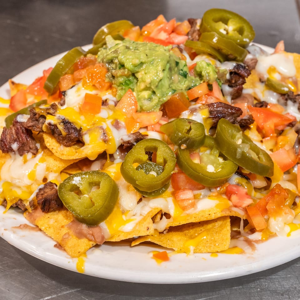 A plate of Casa Mexico nachos with steak, cheese, jalapeños, guacamole, and diced tomatoes.