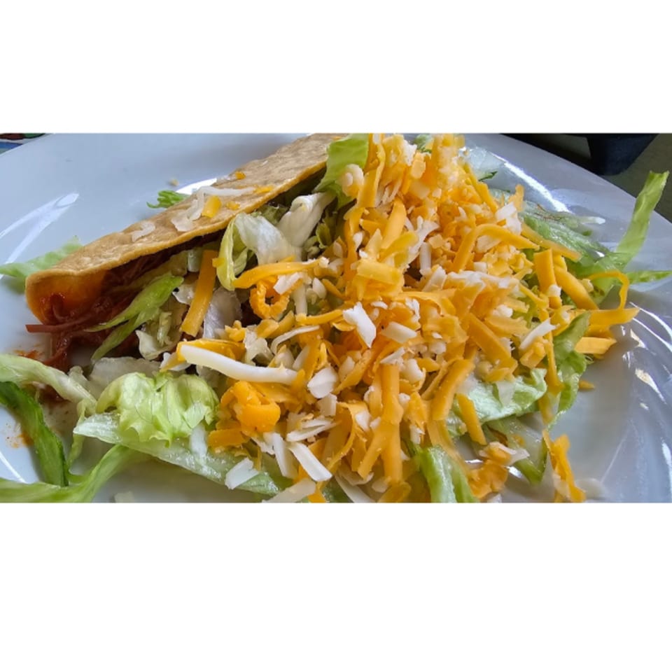 A Casa Mexico taco filled with meat, lettuce, and shredded cheese on a white plate.